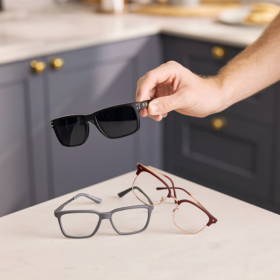 2 pairs of reading glasses sitting on a bench and a person holding a black pair of sunglasses